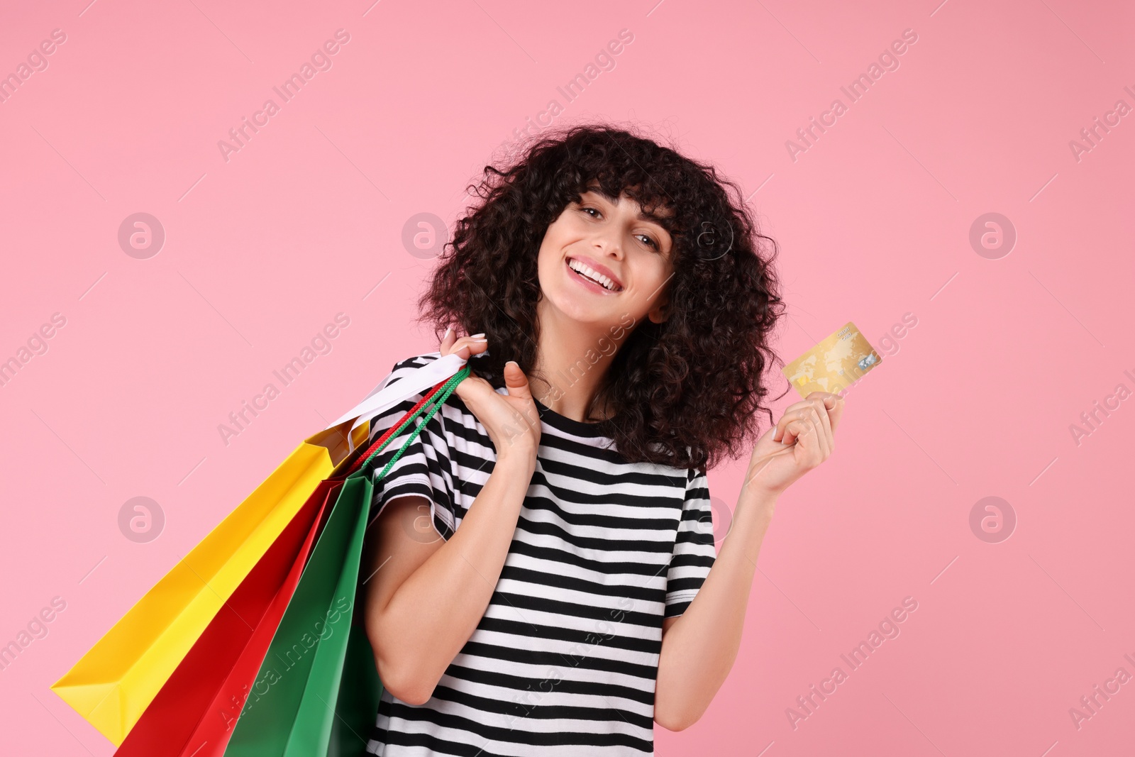Photo of Happy young woman with shopping bags and credit card on pink background