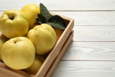 Photo of Fresh ripe organic quinces with leaves on white wooden table, closeup. Space for text