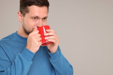 Photo of Man drinking from red mug on grey background. Space for text