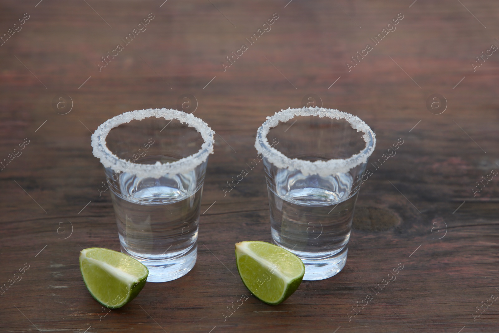 Photo of Mexican tequila shots with lime slices and salt on wooden table