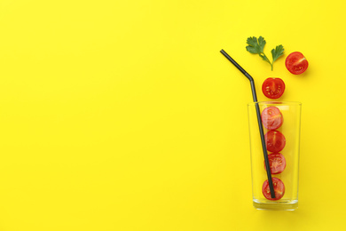 Photo of Glass, fresh tomatoes, parsley and straw on yellow background, flat lay. Space for text