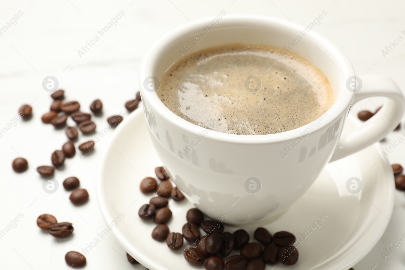 Photo of Cup of aromatic coffee and beans on white table, closeup