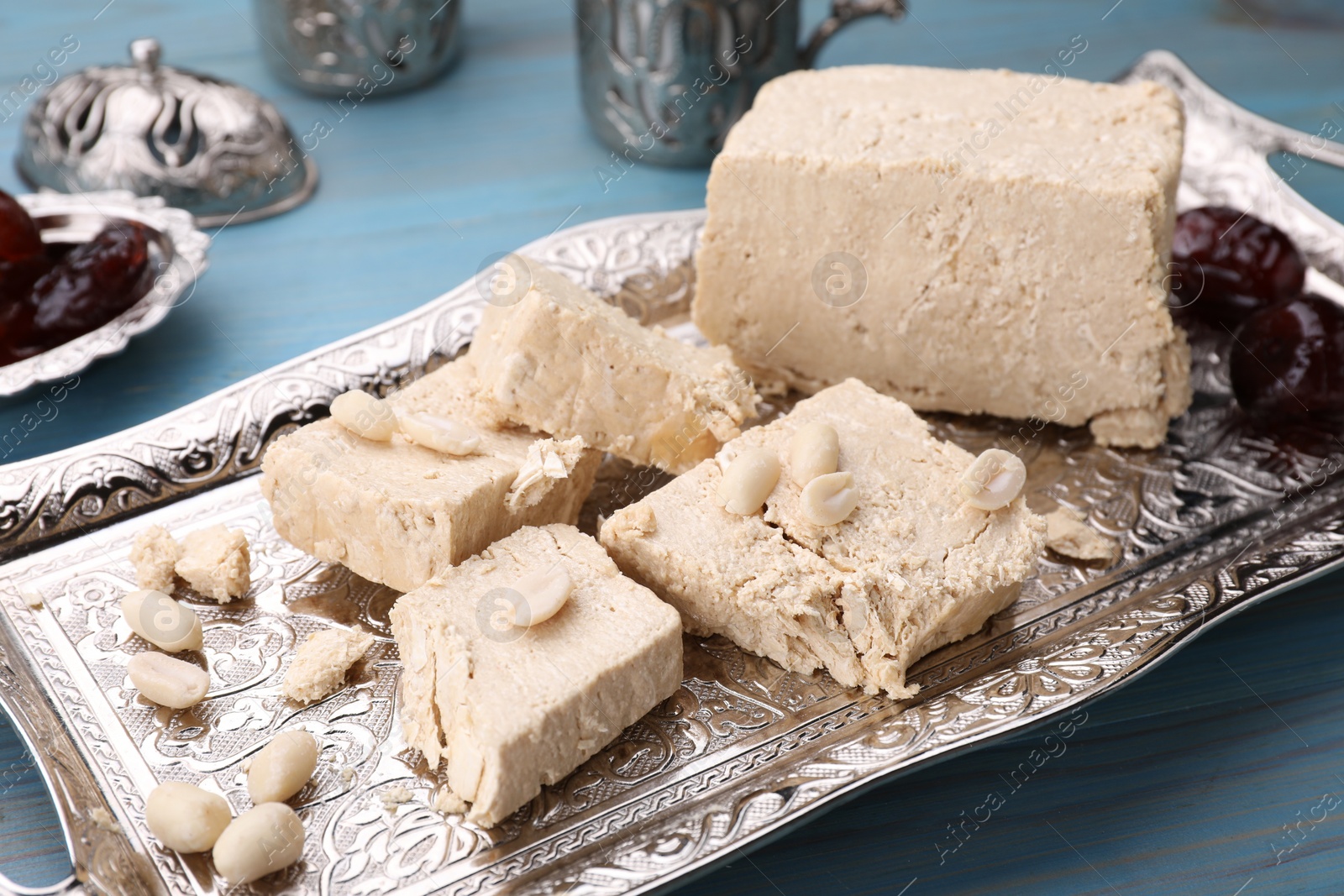 Photo of Pieces of tasty halva and peanuts served on light blue wooden table, closeup