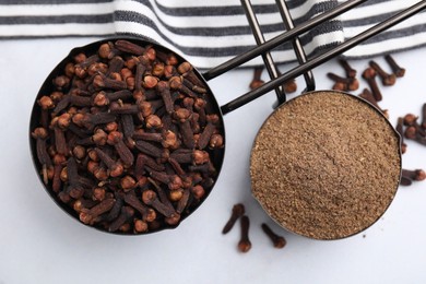 Photo of Aromatic clove powder and dried buds in scoops on white table, top view