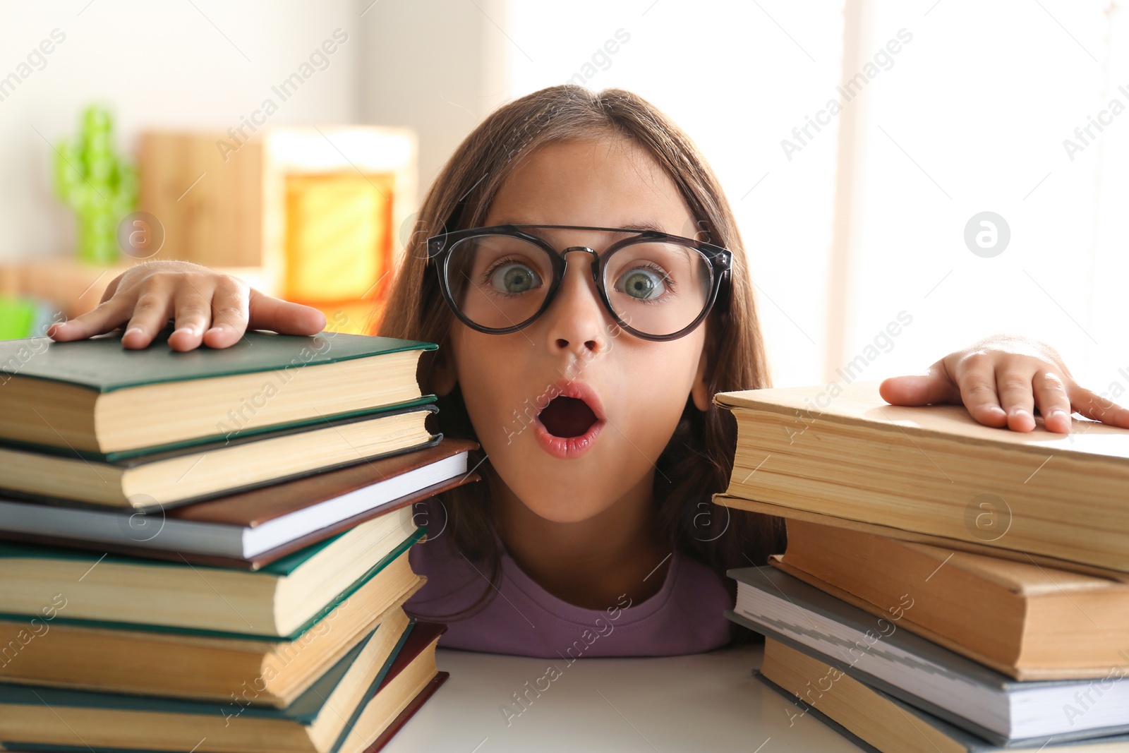 Photo of Emotional little girl at table with books. Doing homework