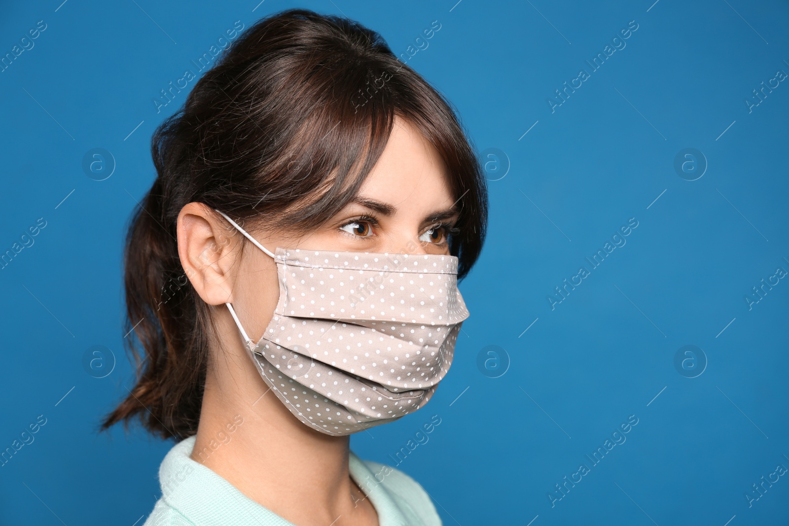 Photo of Young woman in protective face mask on blue background, space for text