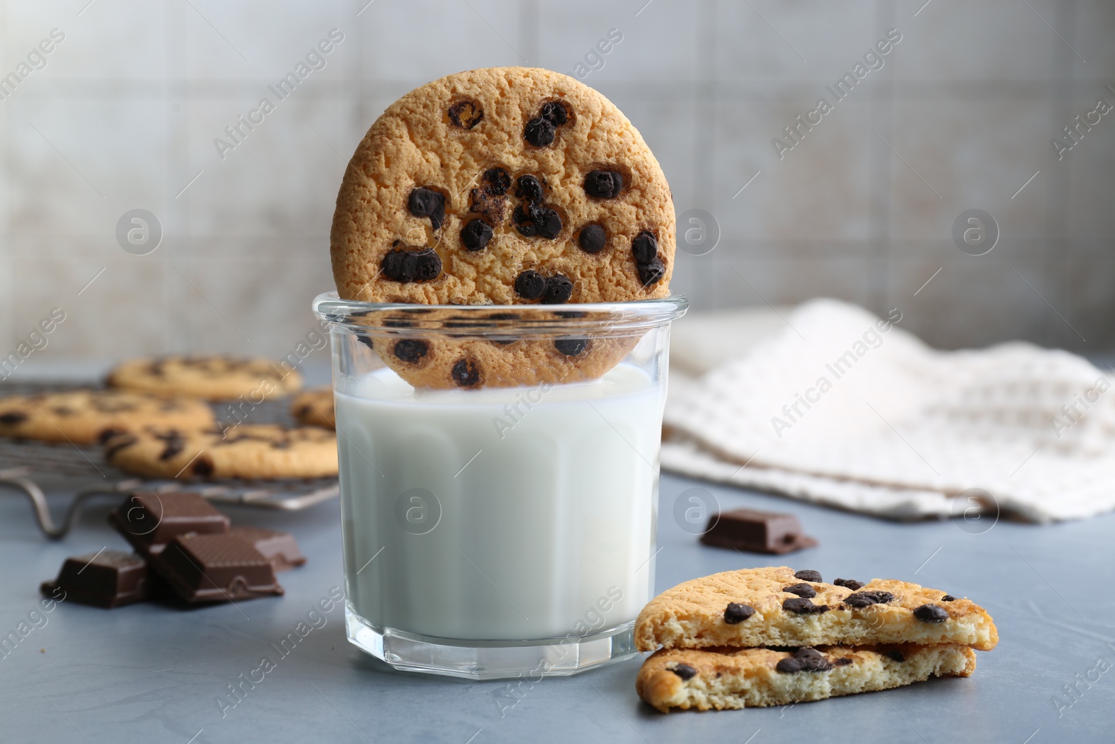 Photo of Delicious chocolate chip cookie dipped into glass of milk at grey table