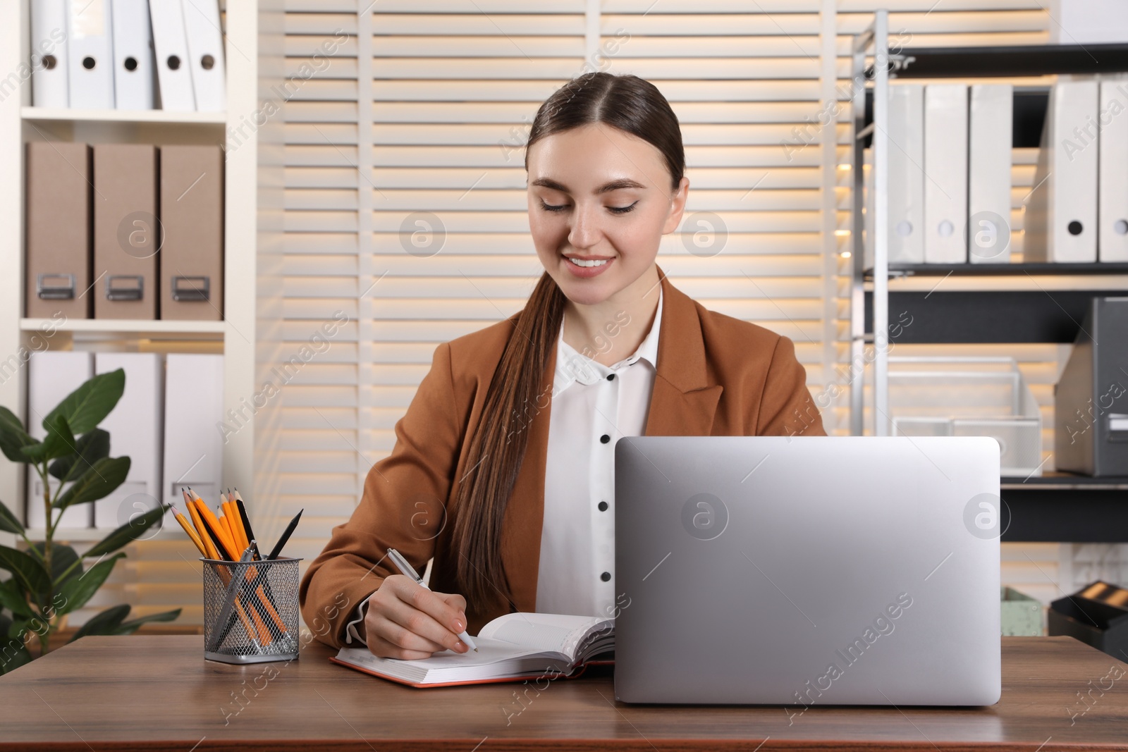 Photo of Happy woman taking notes at wooden table in office