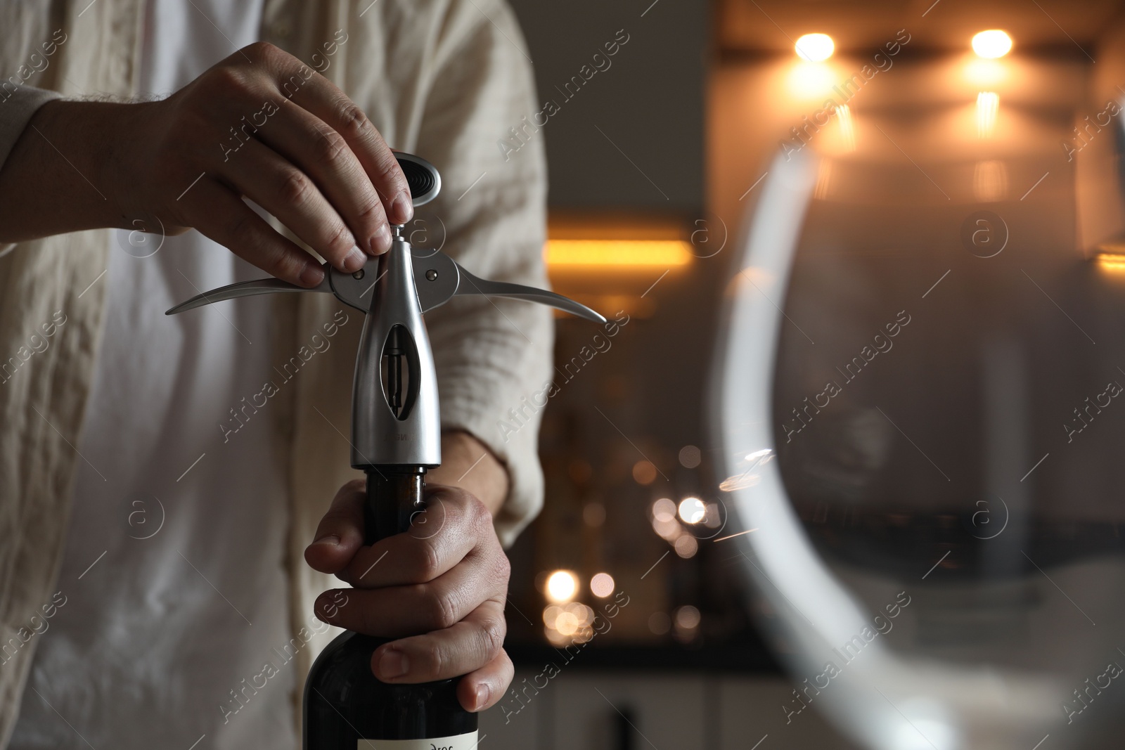 Photo of Man opening wine bottle with corkscrew on blurred background, closeup