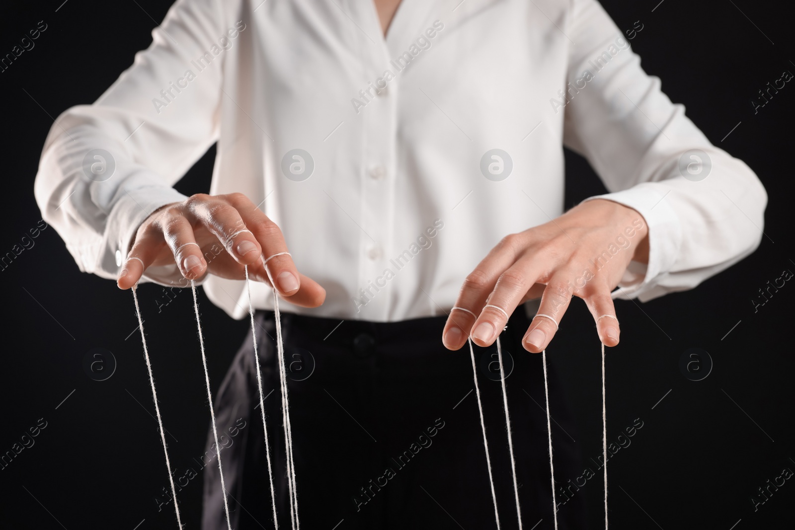 Photo of Woman in formal outfit pulling strings of puppet on black background, closeup