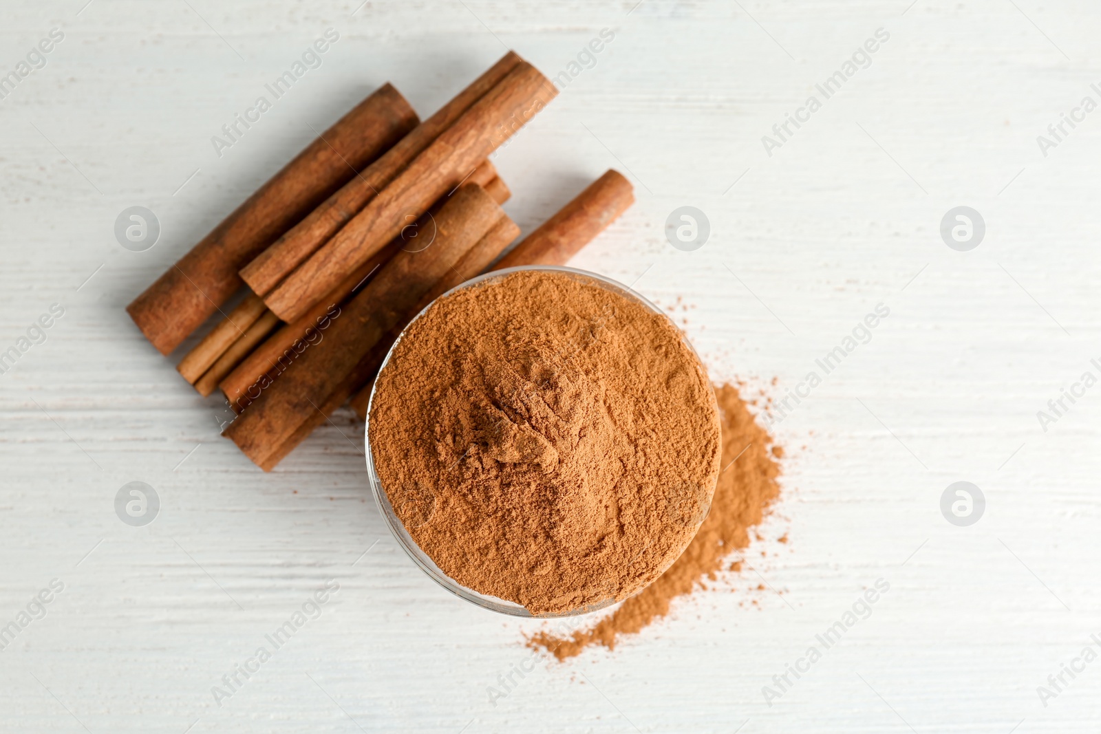 Photo of Bowl with aromatic cinnamon powder and sticks on wooden background