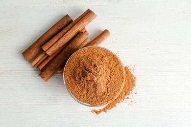 Photo of Bowl with aromatic cinnamon powder and sticks on wooden background