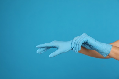 Photo of Doctor wearing medical gloves on light blue background, closeup. Space for text