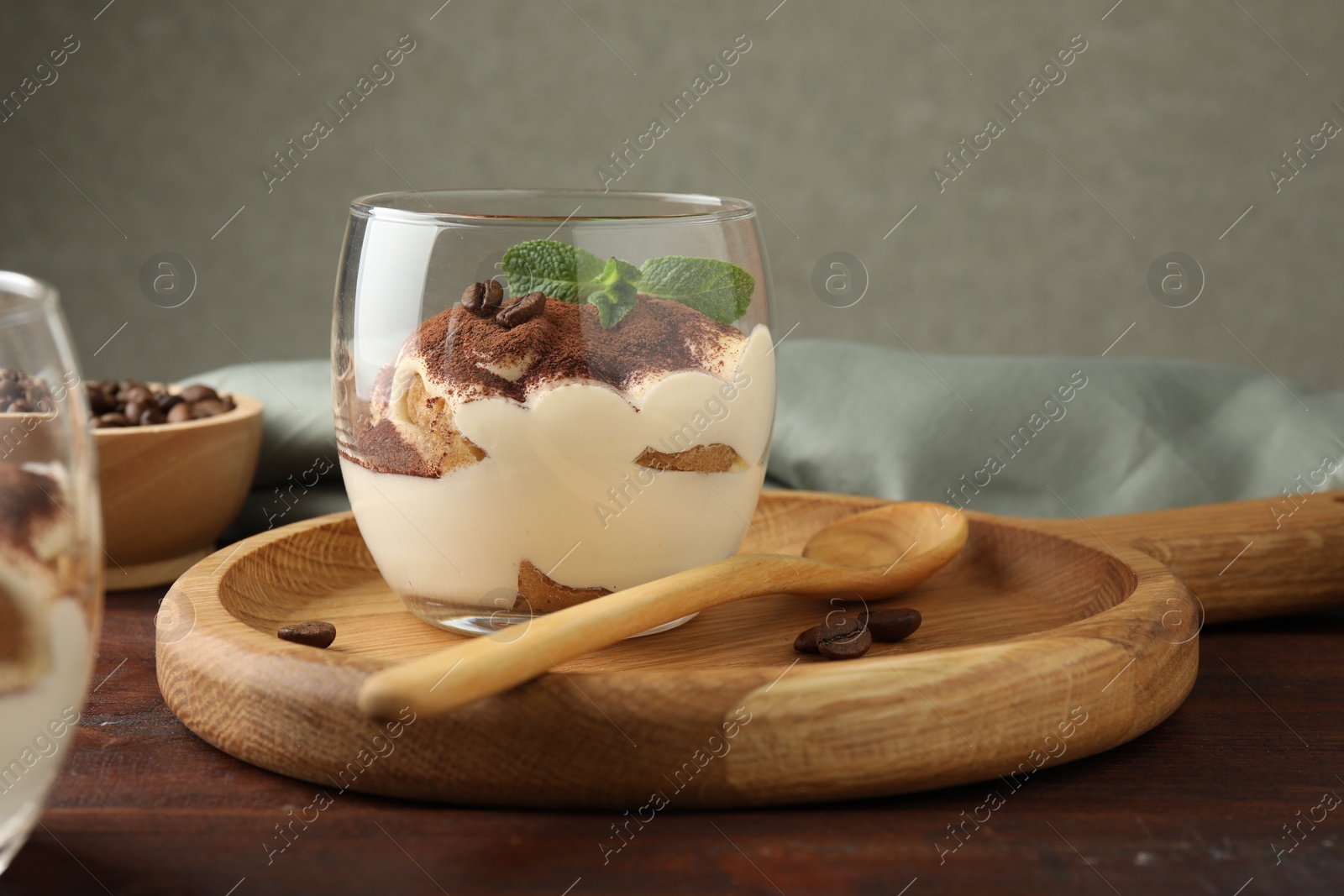 Photo of Delicious tiramisu in glass, mint leaves, coffee beans and spoon on wooden table