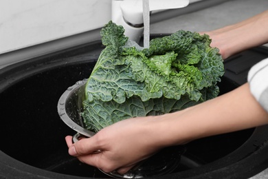 Photo of Woman washing fresh green savoy cabbage under tap water in kitchen sink, closeup