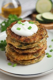 Photo of Delicious zucchini pancakes with sour cream served on white wooden table, closeup
