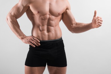 Photo of Young man is stylish black underwear showing thumb up on light grey background, closeup