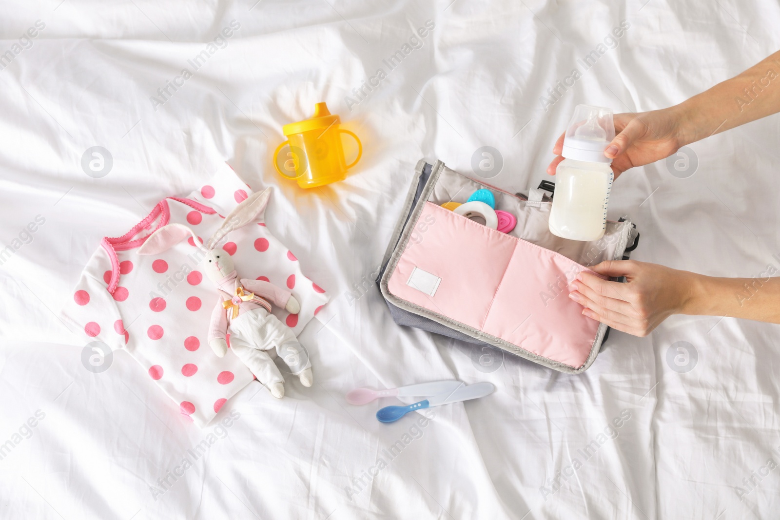 Photo of Woman packing baby accessories into maternity bag on bed, top view