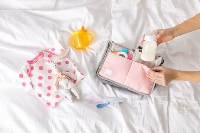 Photo of Woman packing baby accessories into maternity bag on bed, top view