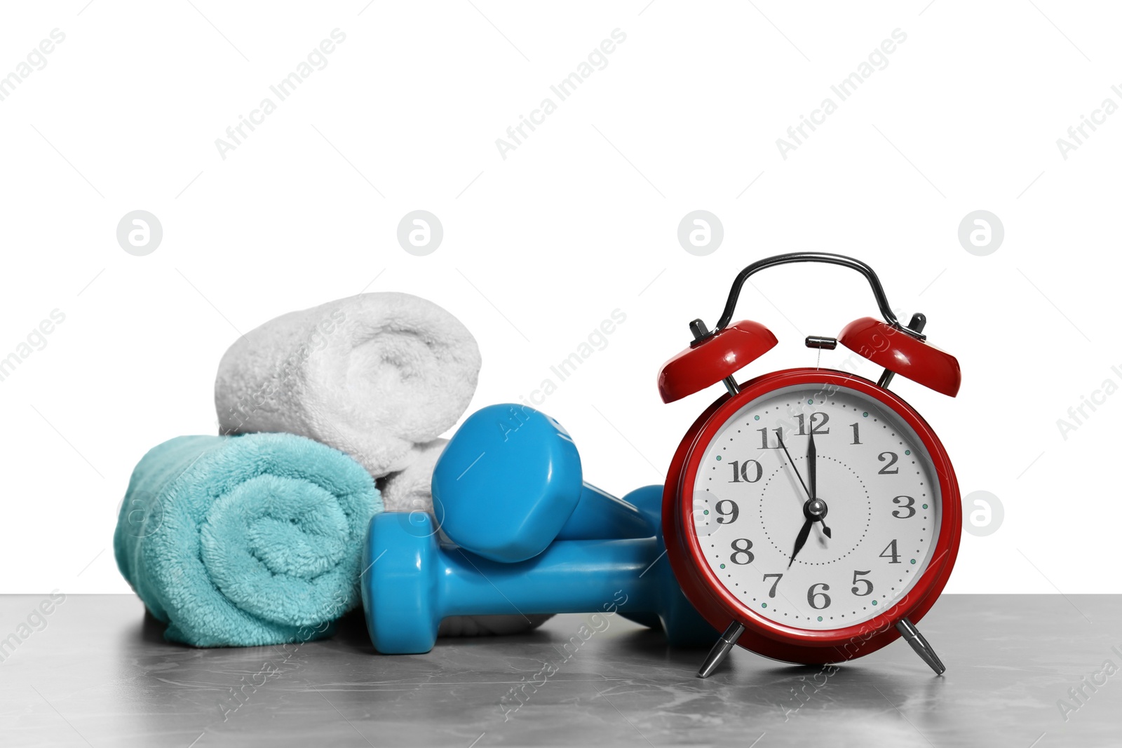 Photo of Alarm clock, towels and dumbbells on marble table against grey background. Morning exercise