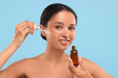 Smiling woman applying serum onto her face on light blue background