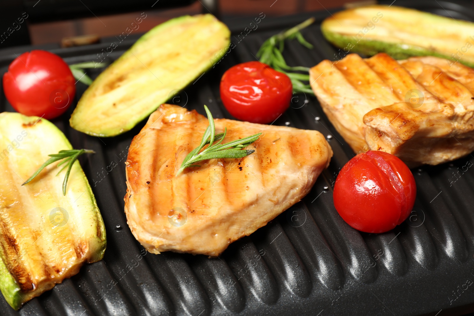 Photo of Tasty meat, rosemary and vegetables on electric grill, closeup