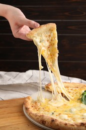 Photo of Woman taking piece of delicious cheese pizza at table, closeup