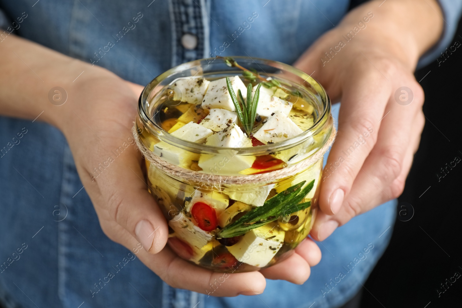 Photo of Woman holding jar with pickled feta cheese on black background, closeup