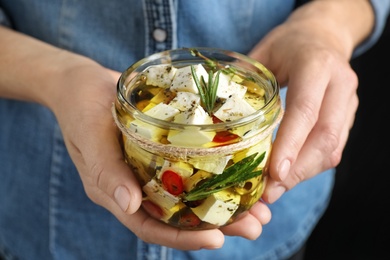 Photo of Woman holding jar with pickled feta cheese on black background, closeup