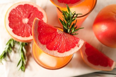 Photo of Tasty grapefruit drink with ice in glasses, rosemary and fresh fruits on light table, top view