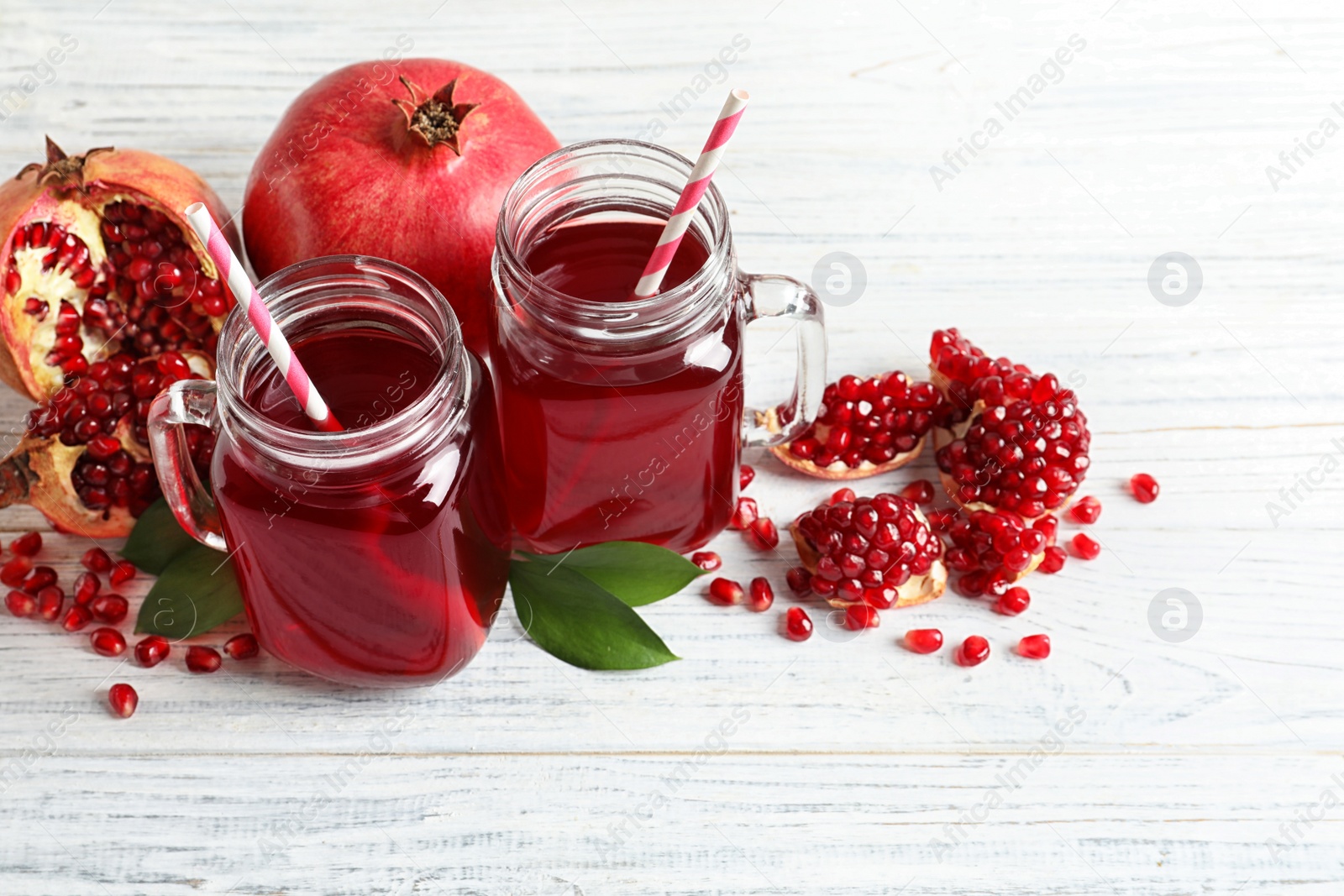 Photo of Mason jars of pomegranate juice and fresh fruits on wooden background, space for text