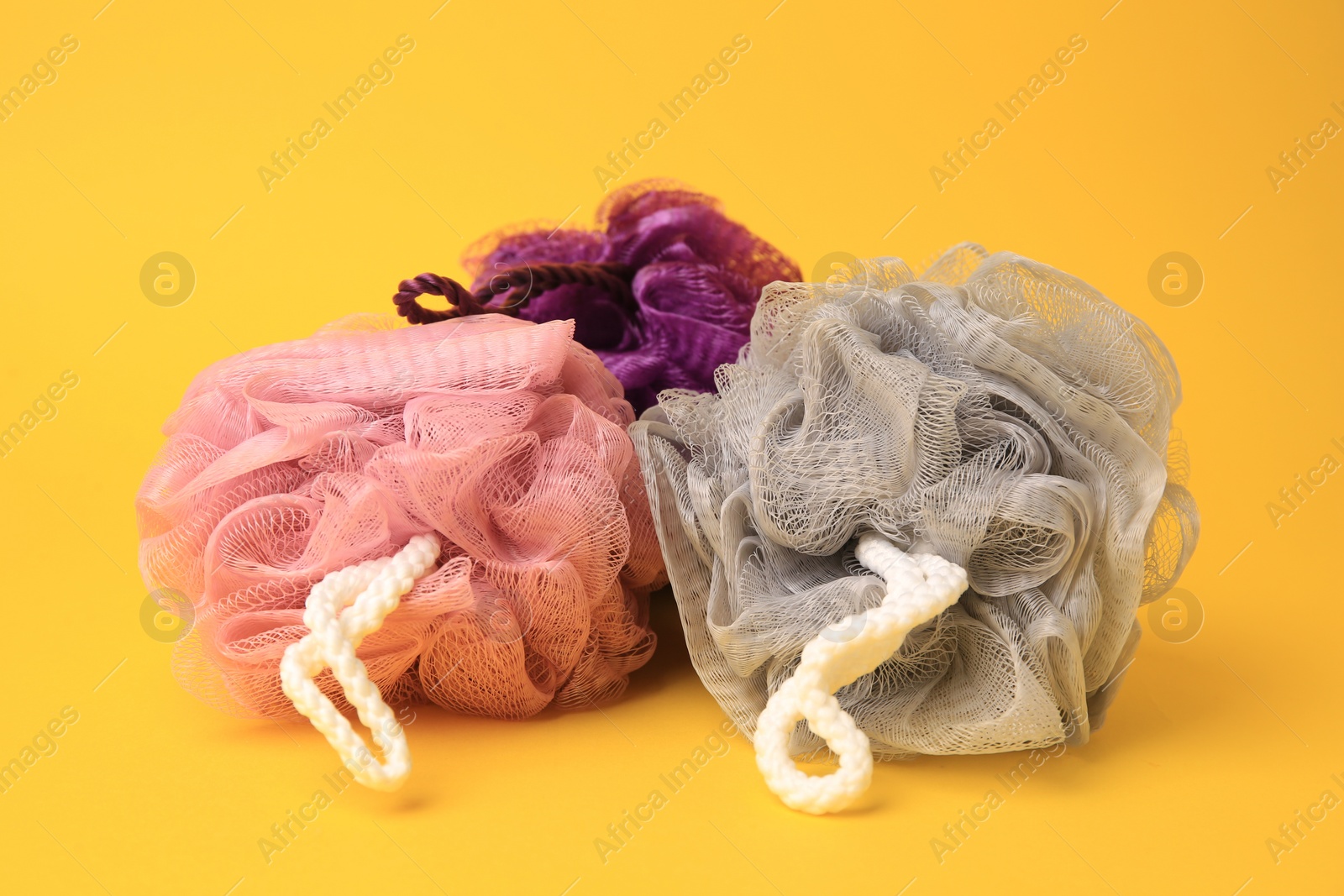 Photo of Colorful shower puffs on yellow background. Personal hygiene