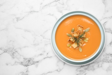 Photo of Tasty creamy pumpkin soup with croutons, seeds and dill in bowl on white marble table, top view. Space for text