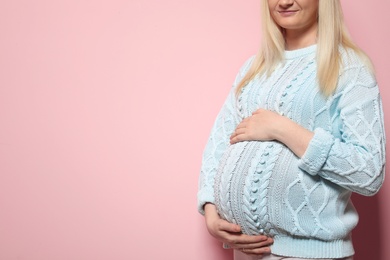 Pregnant woman in sweater on color background. Space for text