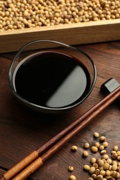 Photo of Soy sauce in bowl, soybeans and chopsticks on wooden table