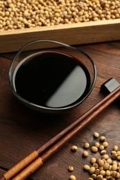 Soy sauce in bowl, soybeans and chopsticks on wooden table