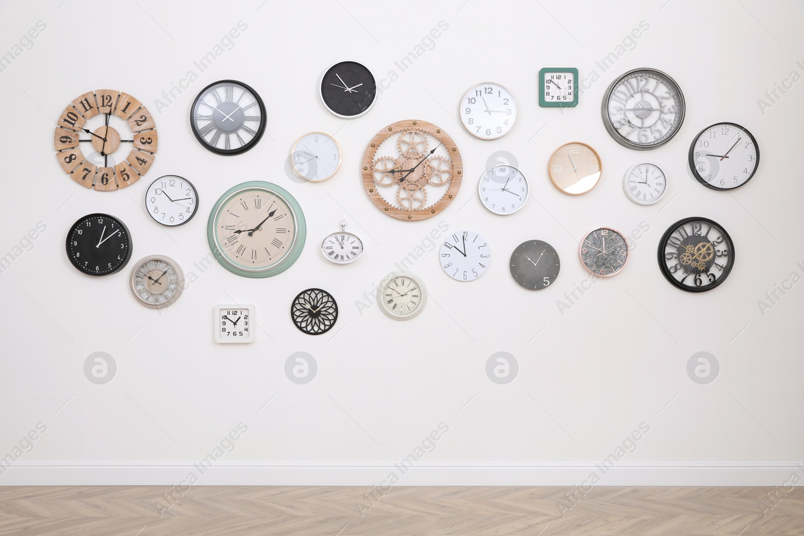 Photo of Collection of different clocks hanging on white wall in room