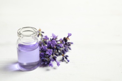 Photo of Bottle of essential oil and lavender flowers on white wooden table. Space for text