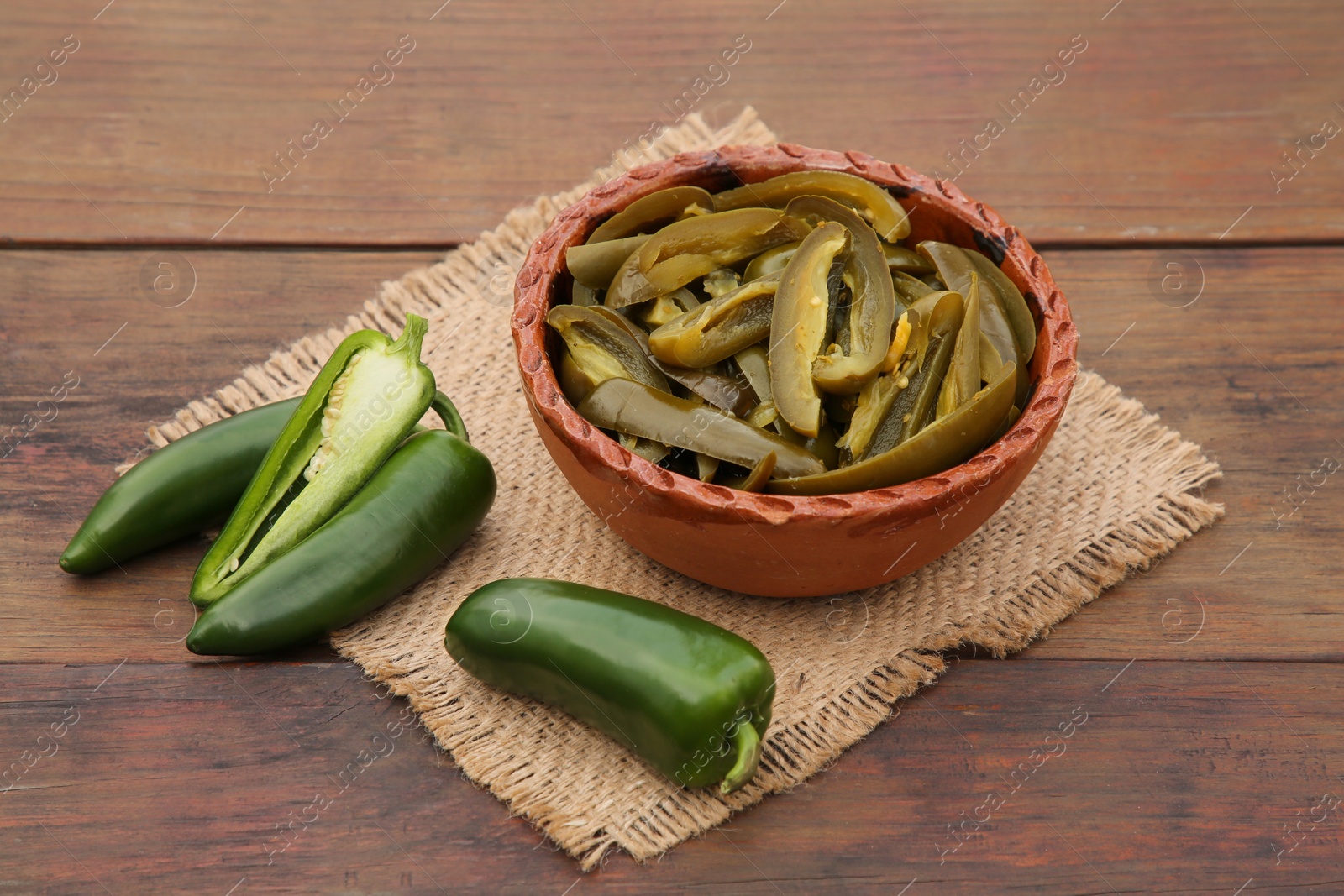 Photo of Fresh and pickled green jalapeno peppers on wooden table