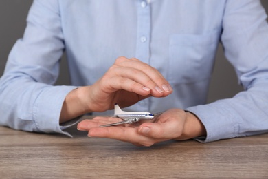 Photo of Insurance agent covering toy plane at table, closeup. Travel safety concept