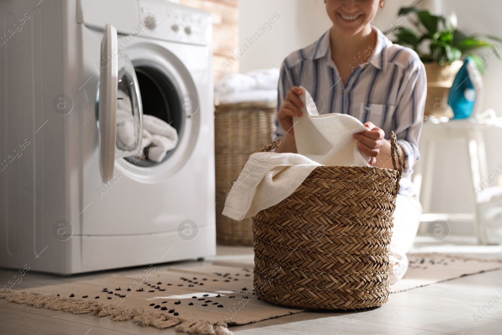 Photo of Young woman with laundry basket near washing machine at home