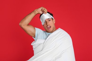 Photo of Man in sleeping mask wrapped with blanket on red background