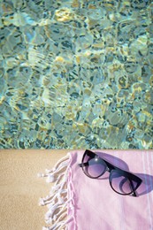 Stylish sunglasses and blanket near outdoor pool on sunny day, above view. Space for text