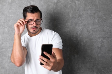 Young man with glasses using mobile phone on grey background, space for text. Vision problem