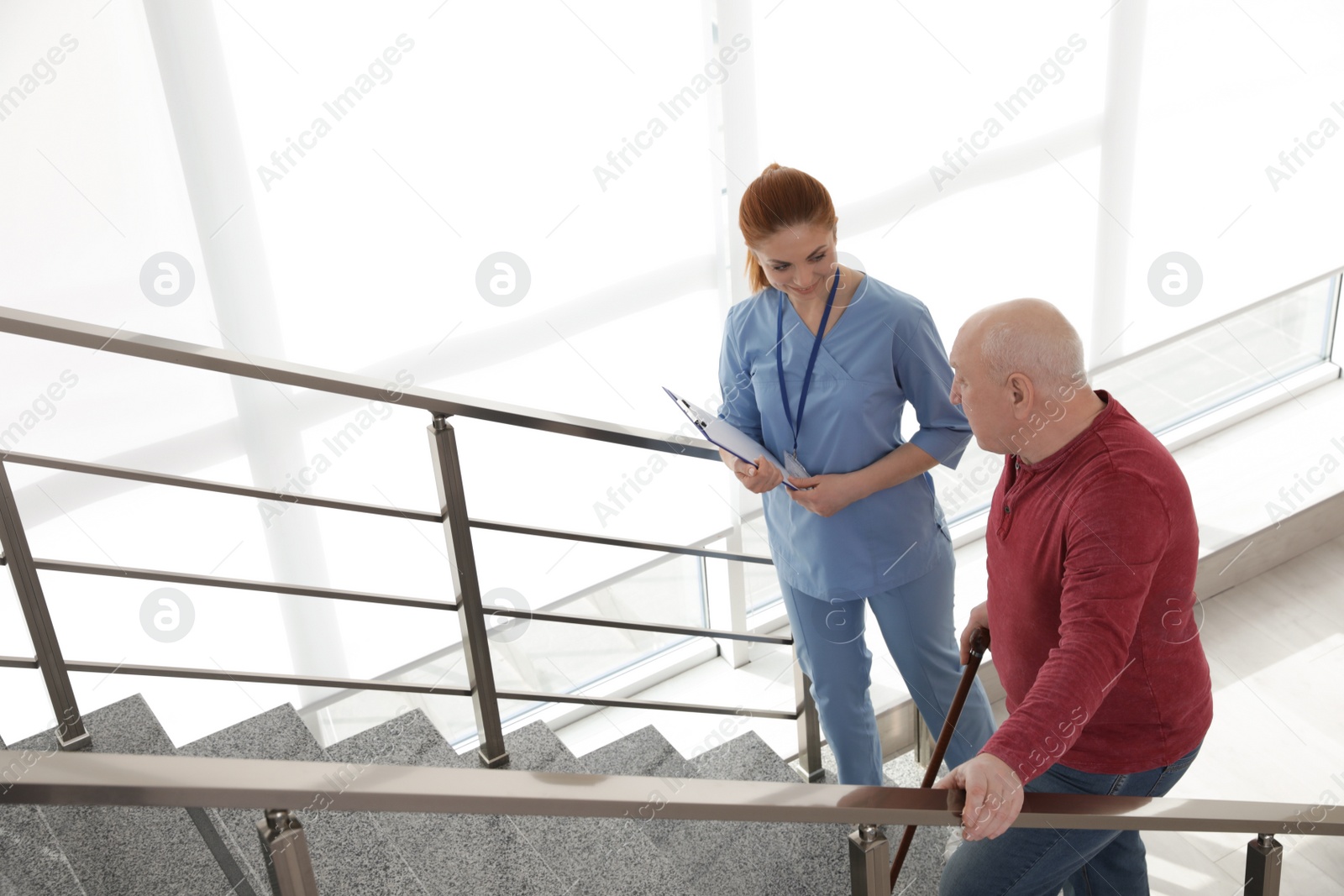 Photo of Nurse assisting senior man with cane to go up stairs indoors