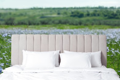 Image of Comfortable bed with soft pillows in beautiful blooming flax field