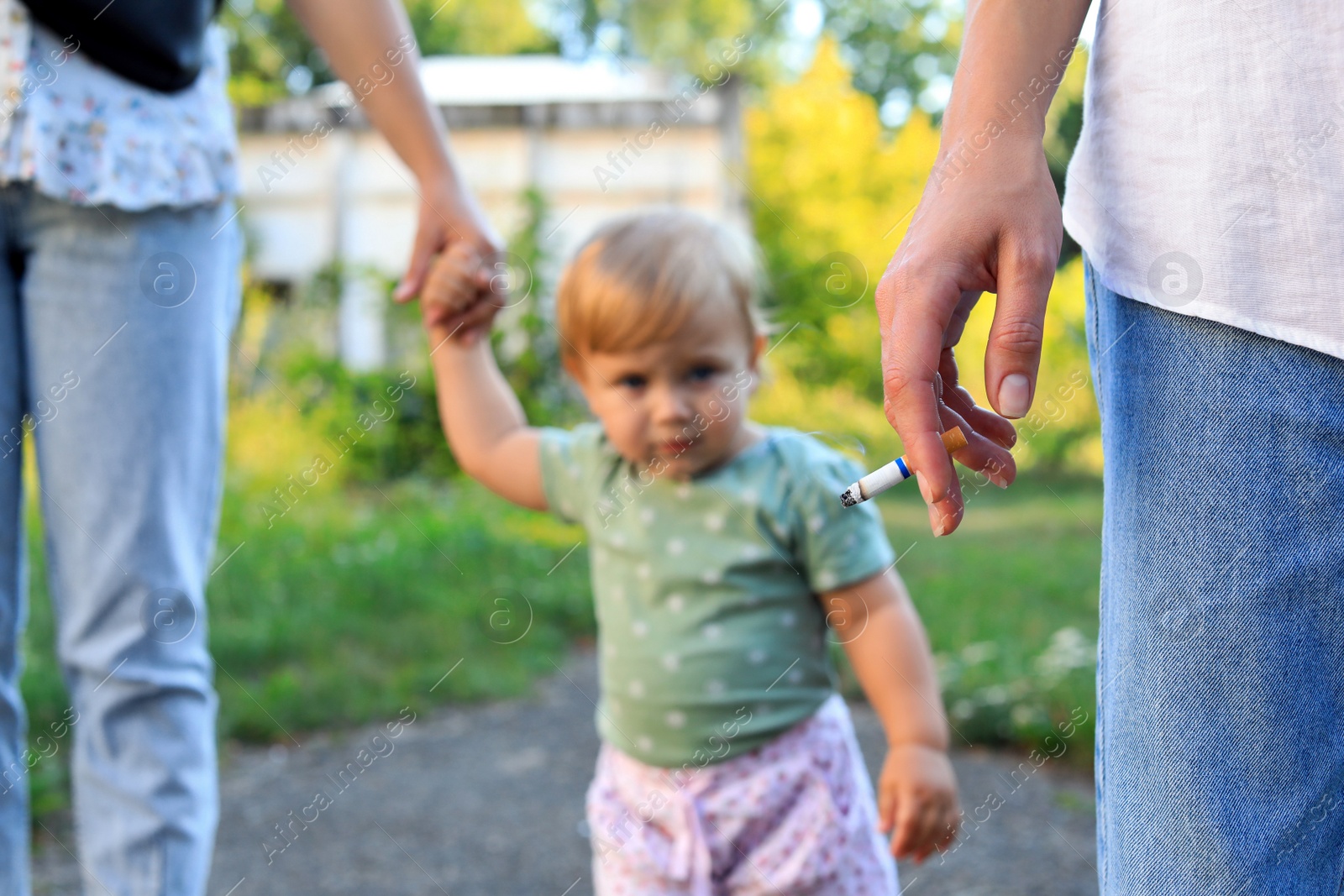 Photo of Woman smoking cigarette in public place outdoors, closeup. Don't smoke near kids