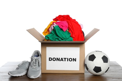 Donation box with clothes, shoes and soccer ball on table against white background