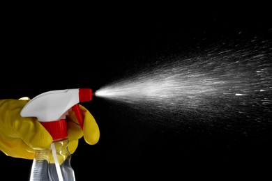 Photo of Woman spraying liquid from bottle on black background, closeup