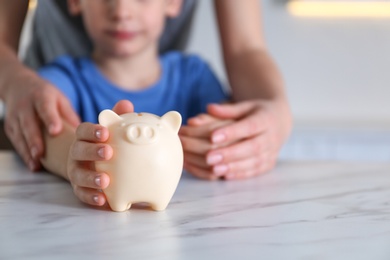 Photo of Mother and son with piggy bank at marble table indoors, closeup